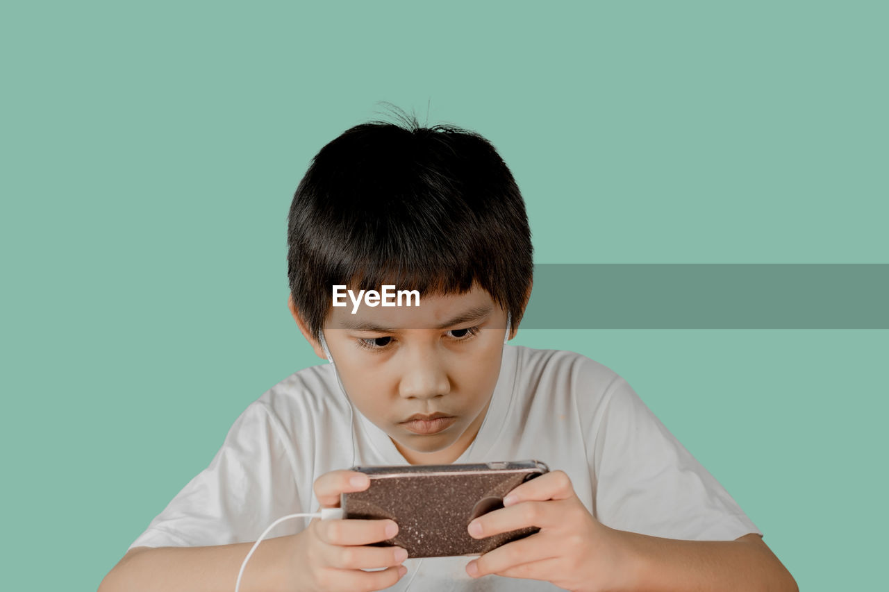 PORTRAIT OF BOY HOLDING CAMERA OVER GRAY BACKGROUND