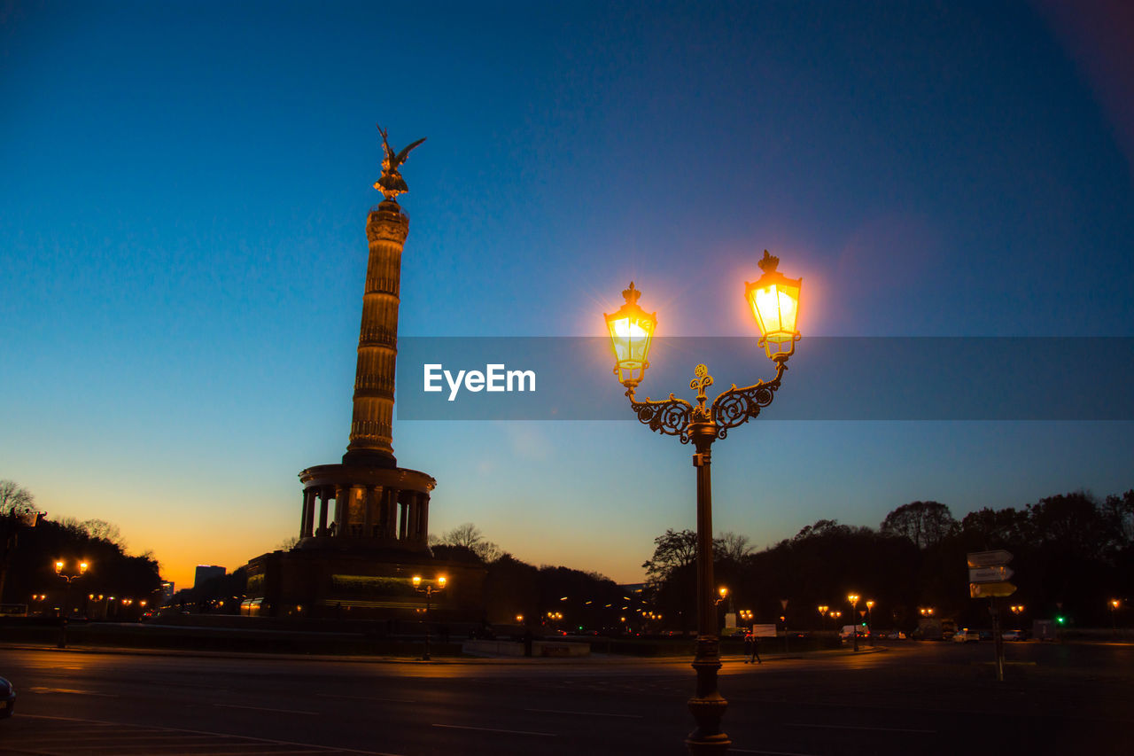 Victory column and illuminated street light against sky at night