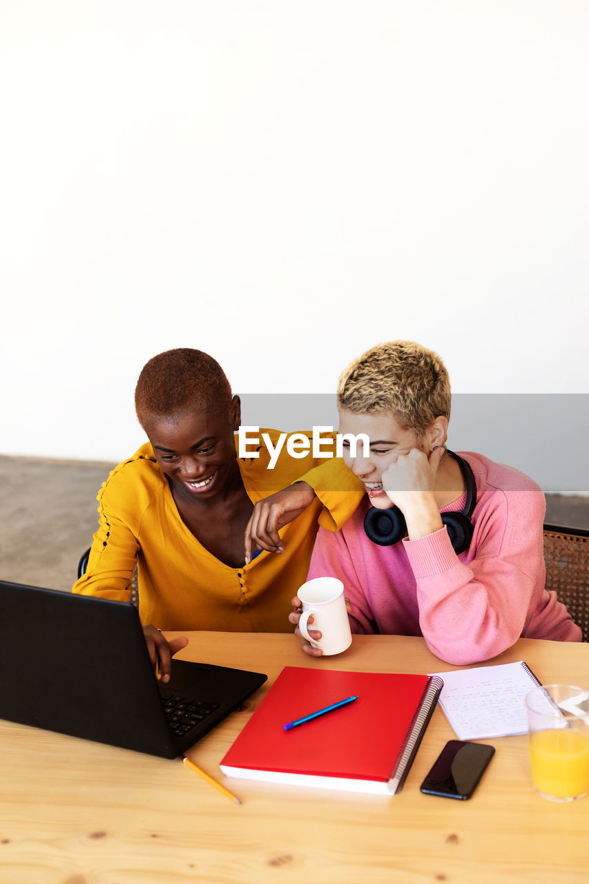 Cheerful lesbian couple working over laptop on table at home