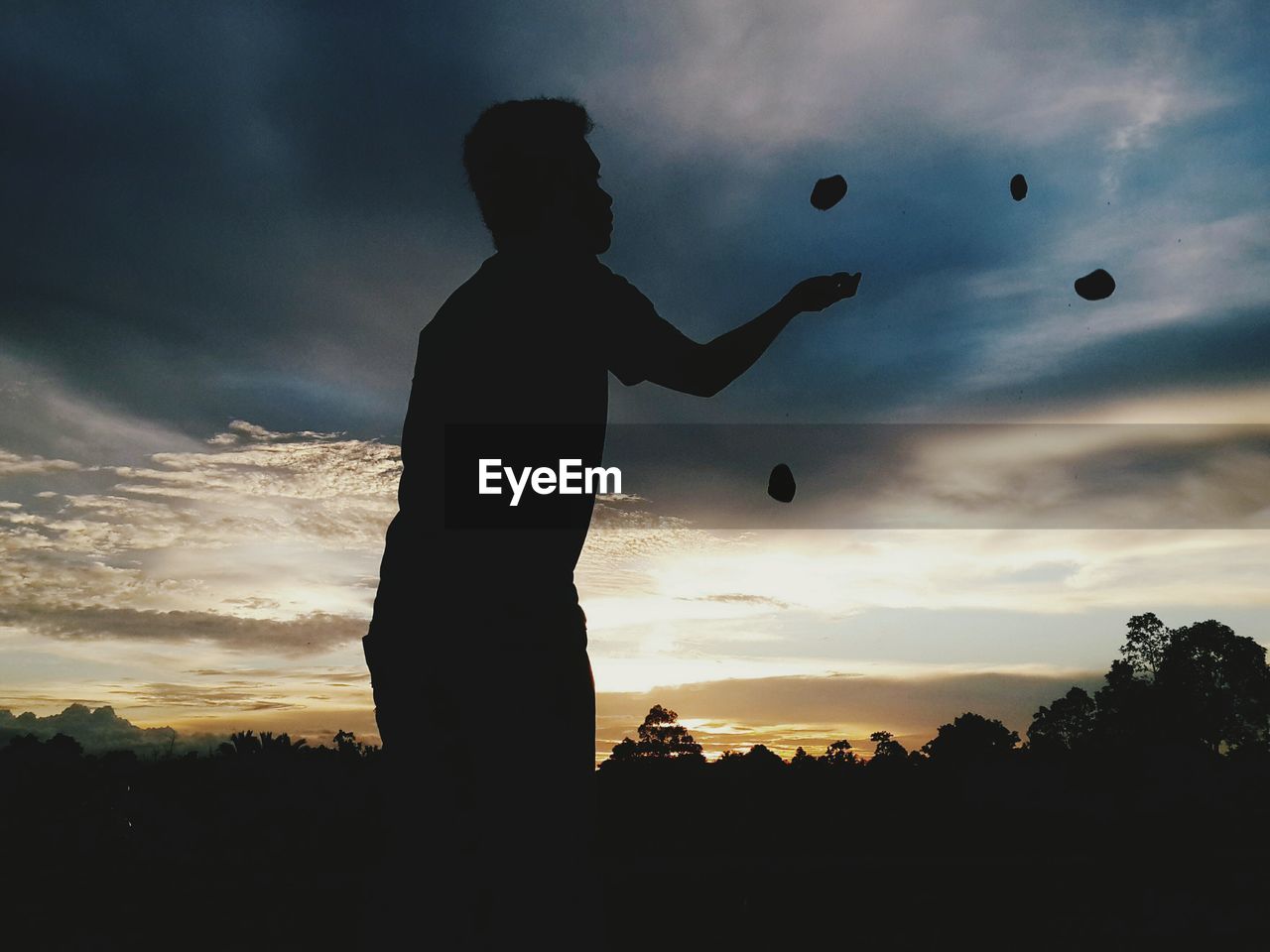 Silhouette man juggling with stone against sky