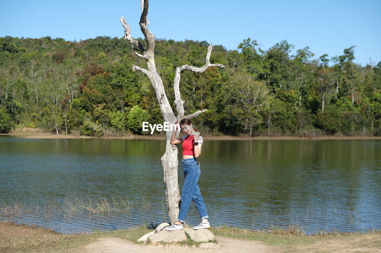 Rear view of woman with arms outstretched standing by lake