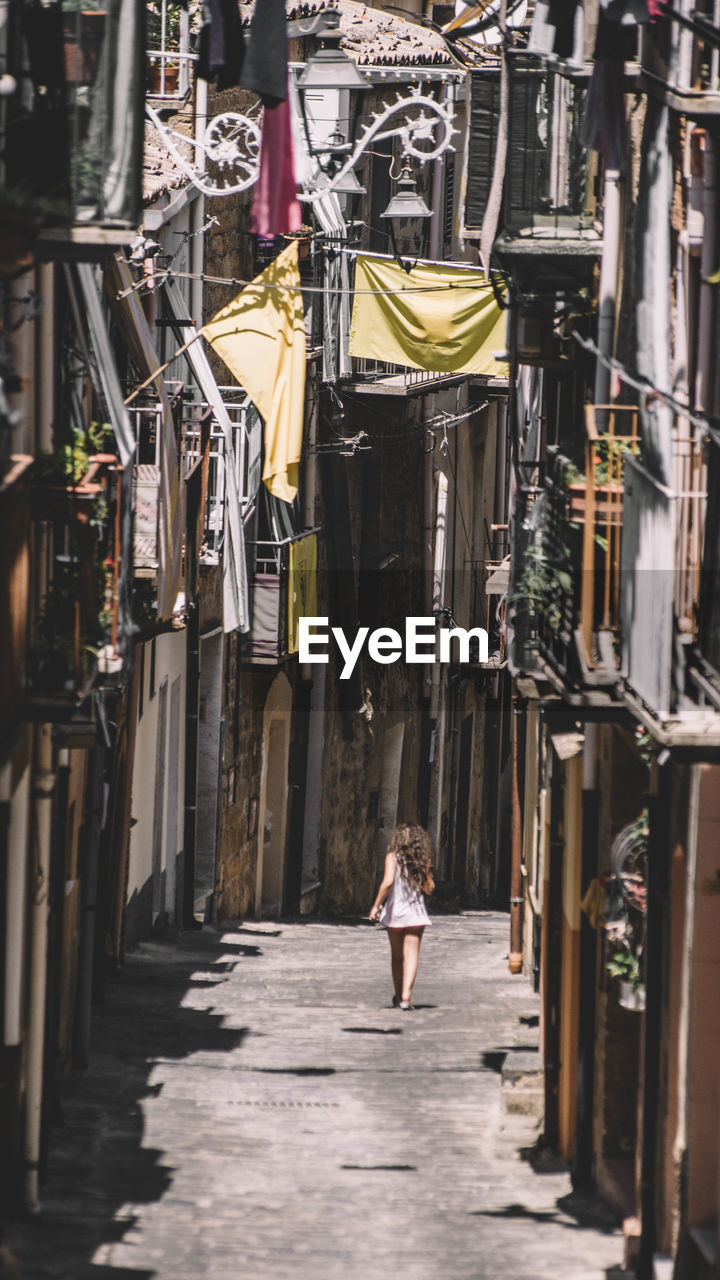 Rear view of woman walking on footpath amidst buildings