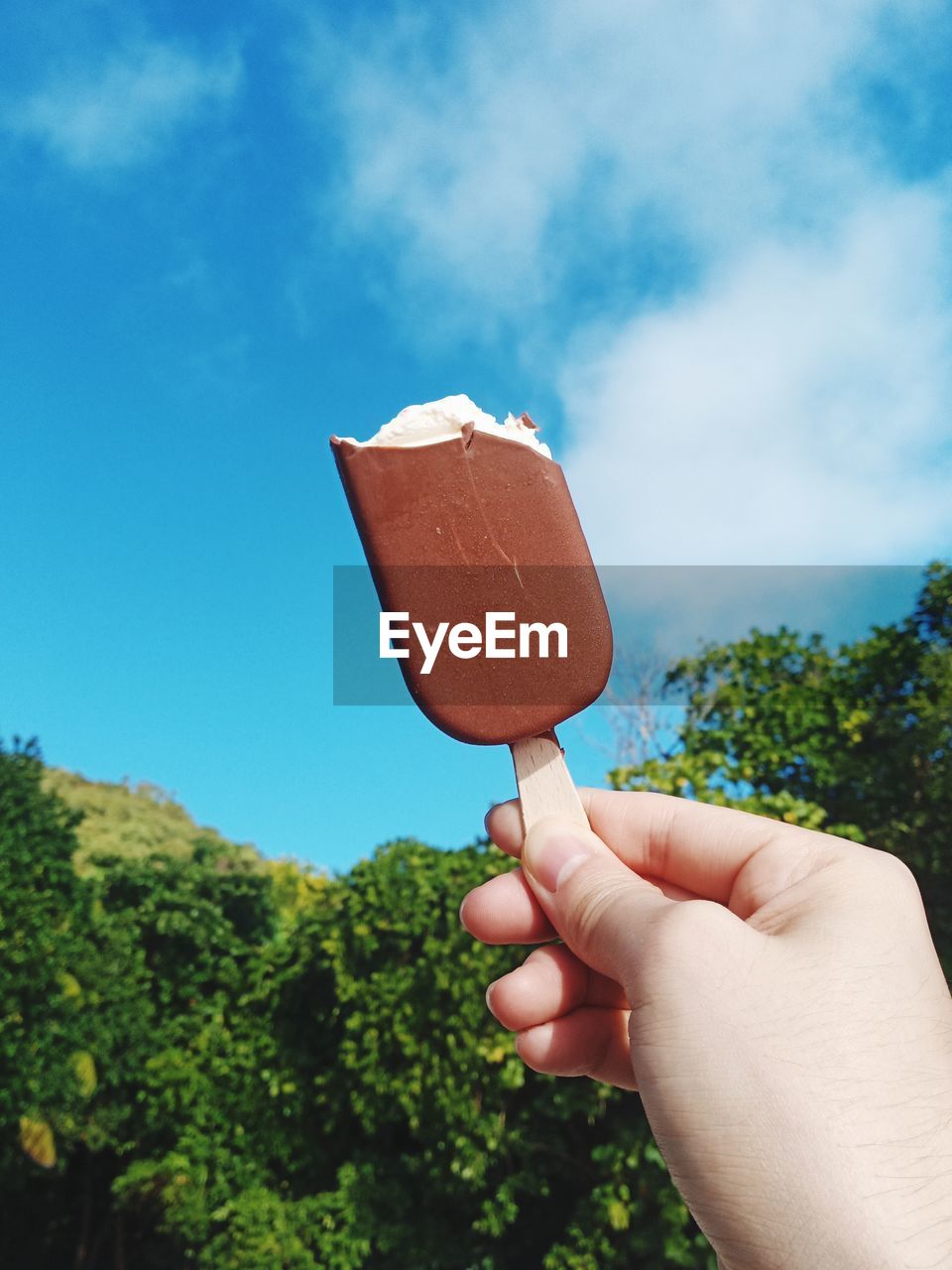 PERSON HOLDING ICE CREAM CONE AGAINST SKY