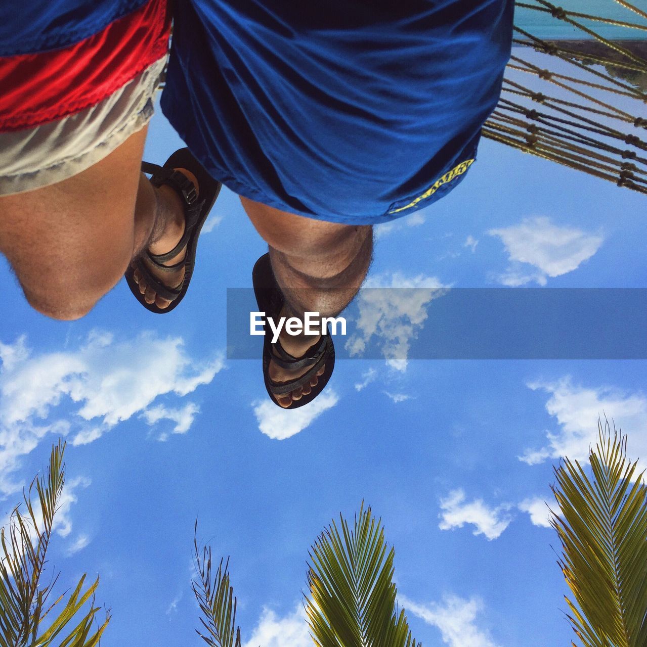 Low section of man relaxing on hammock against blue sky