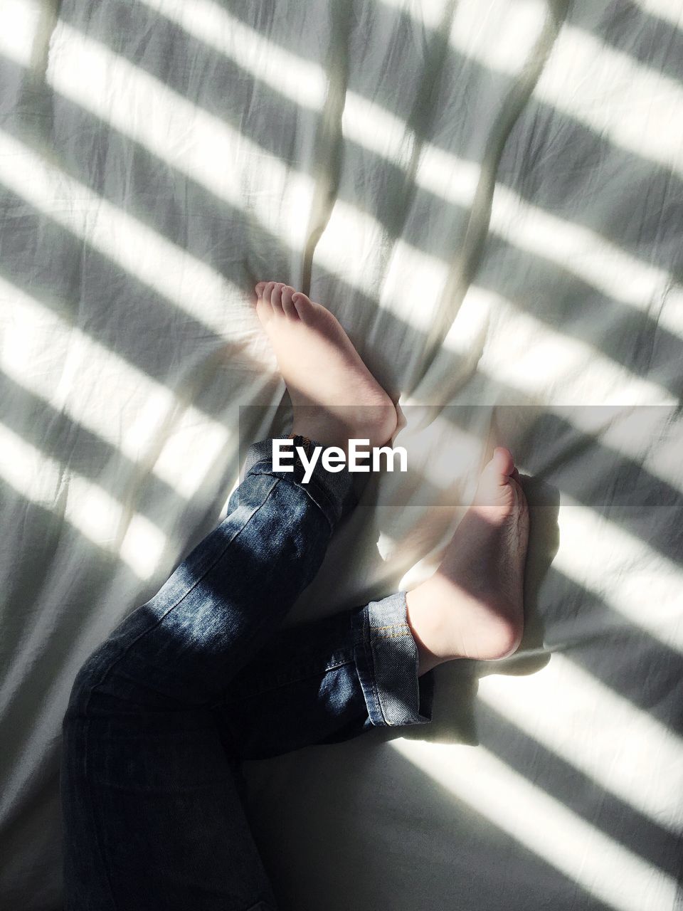 Low section of kid sleeping on bed with shadow