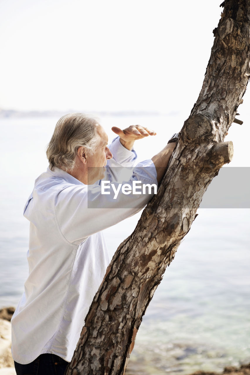 Senior man shielding eyes while looking at view