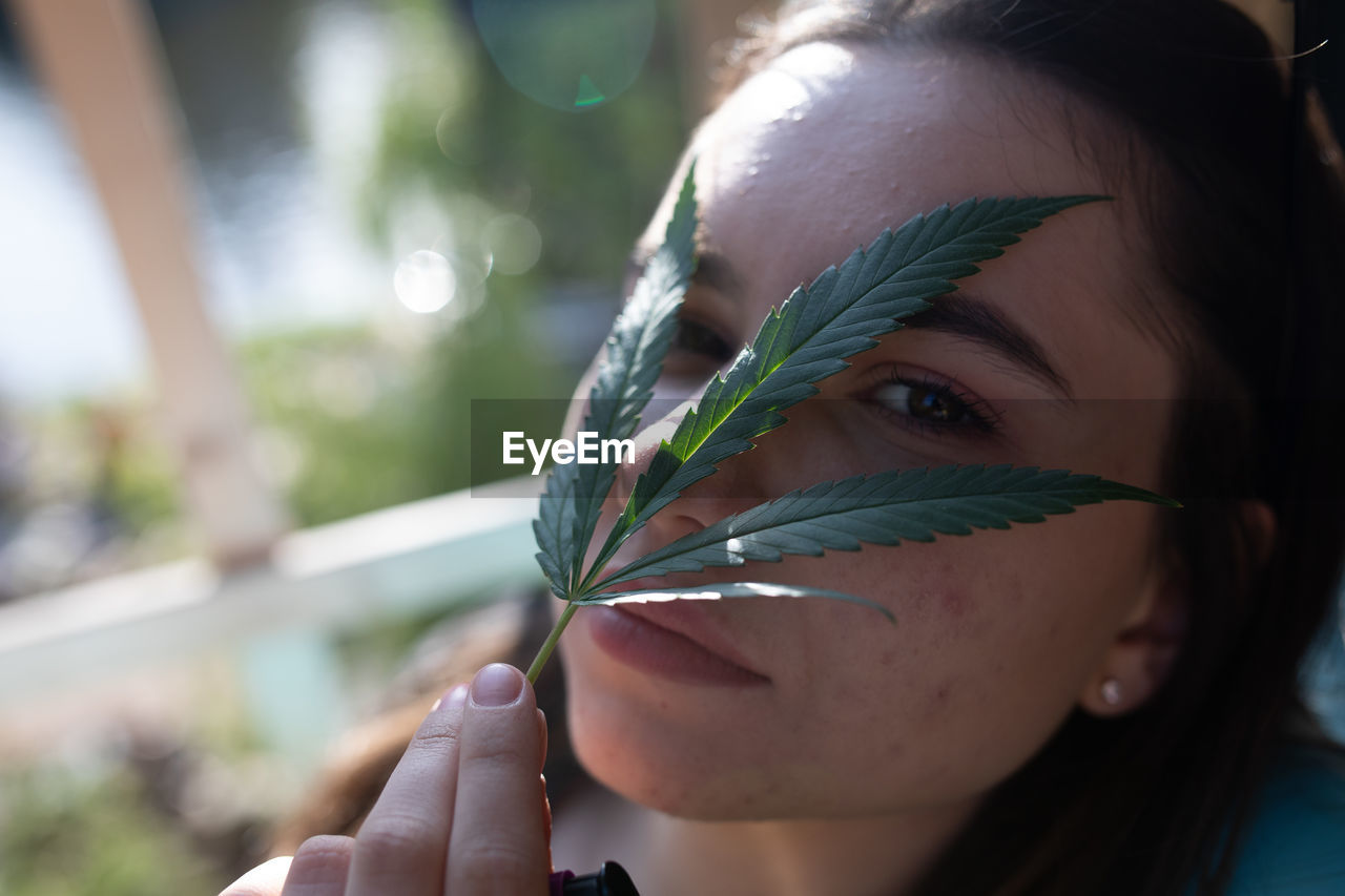 Close-up portrait of young woman holding leaves over face