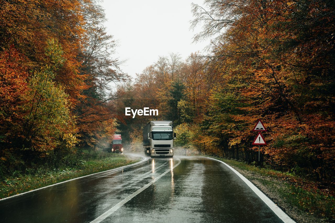 Trucks on road amidst trees during autumn