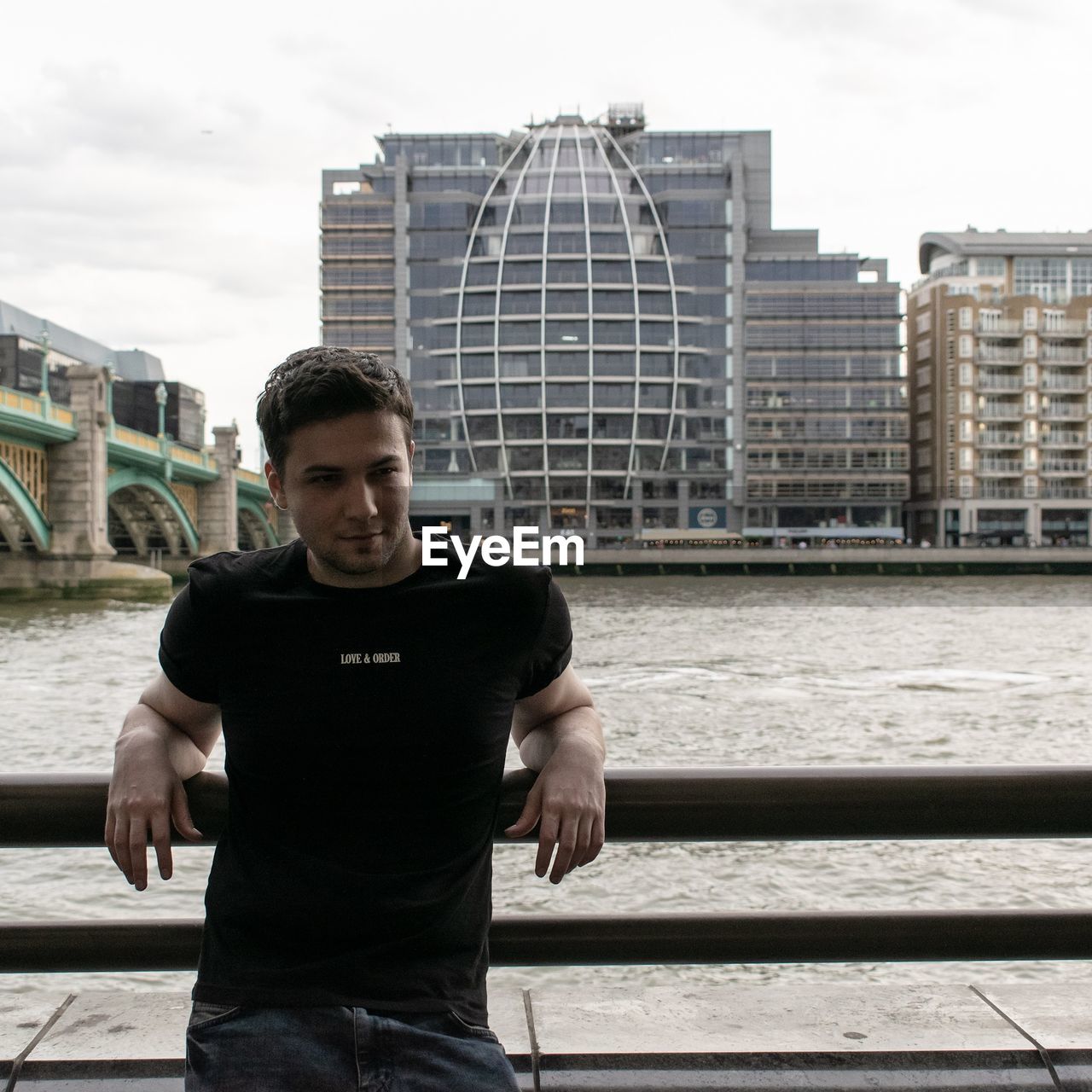 Young man standing by river against buildings in city