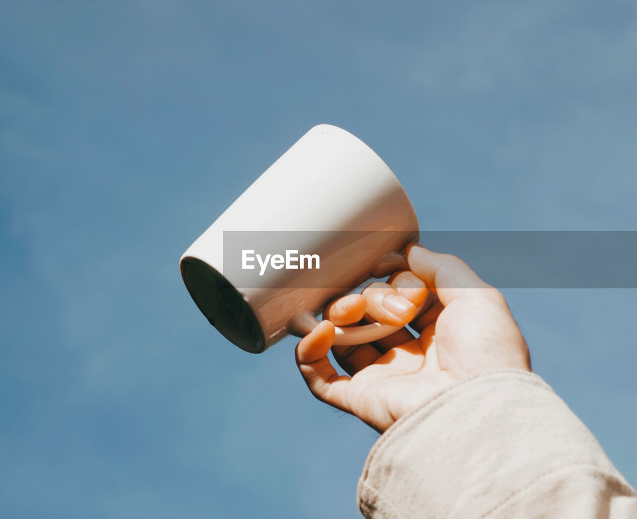 Low angle view of person holding cup camera against sky