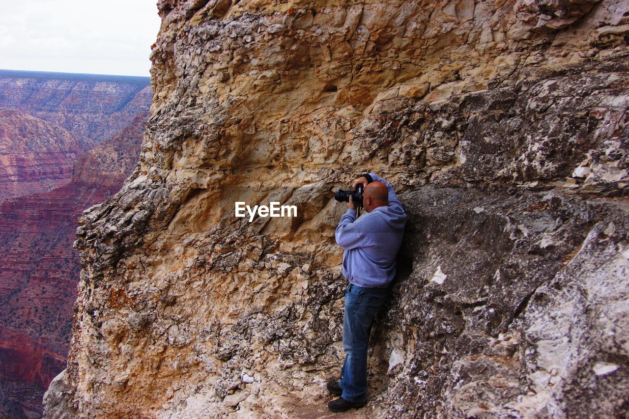 Side view of man photographing through camera while standing on mountain