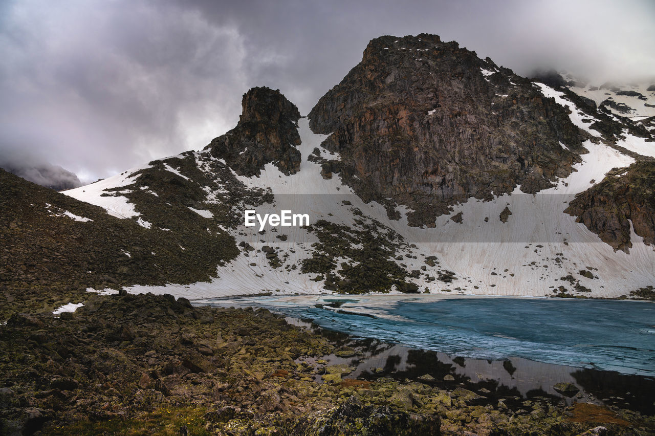 Calm landscape with snowy mountains in the clouds and mountain lakes in ice. mystical rocky