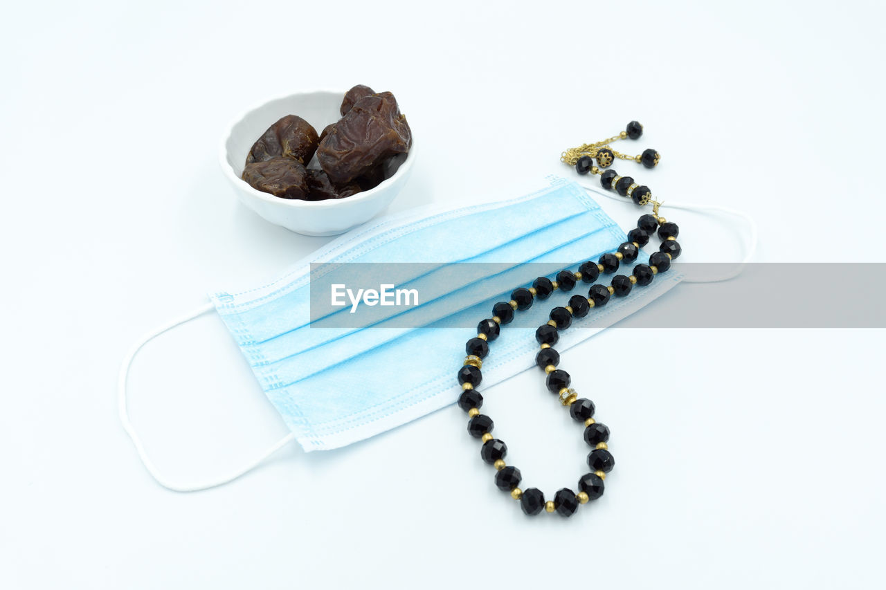 High angle view of surgical face mask, dates and rosary over white background