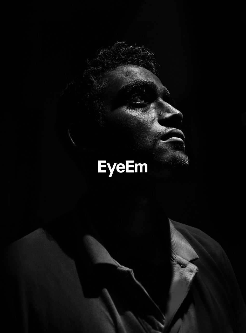 Thoughtful young man looking away against black background