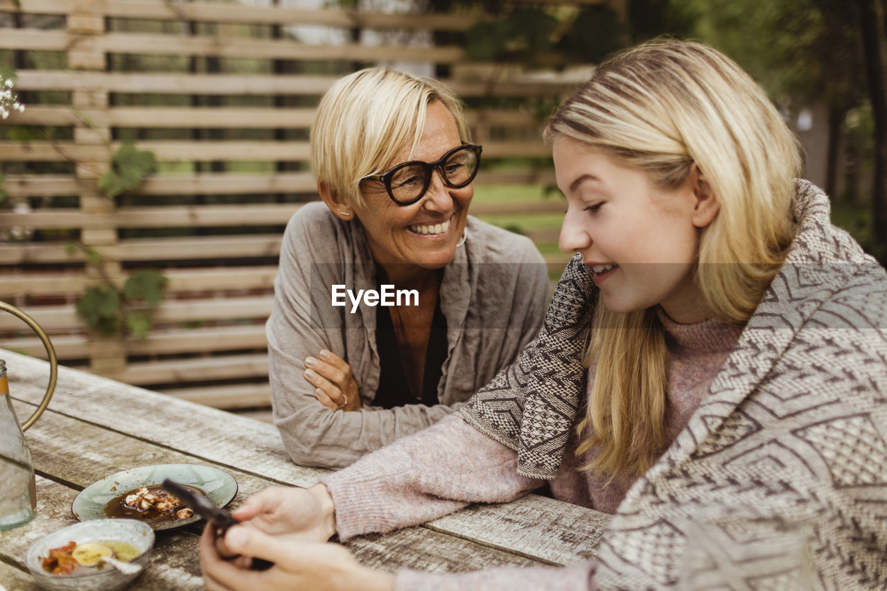 Happy grandmother looking at granddaughter using mobile phone in back yard