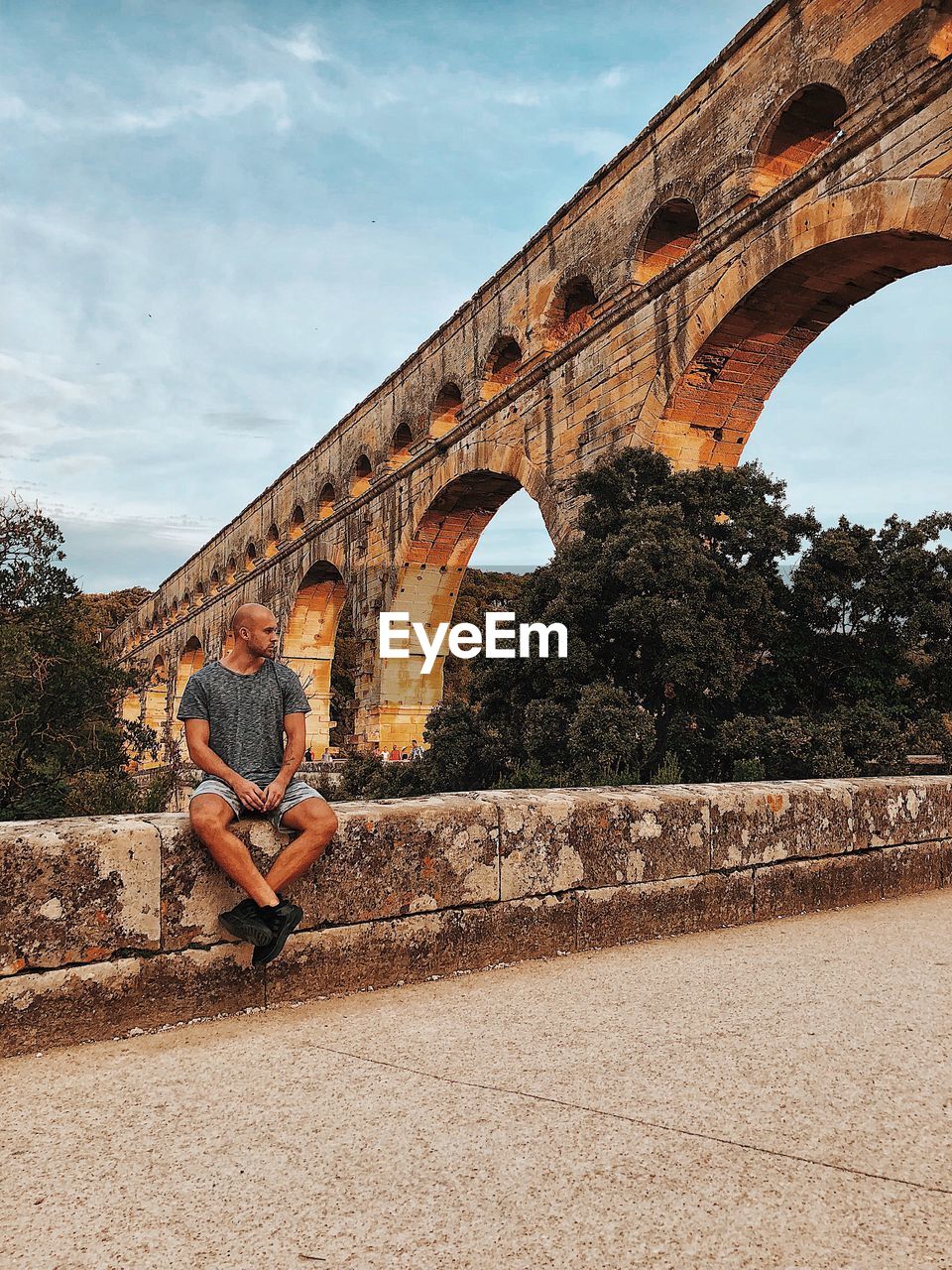 Woman sitting on railing against arch bridge