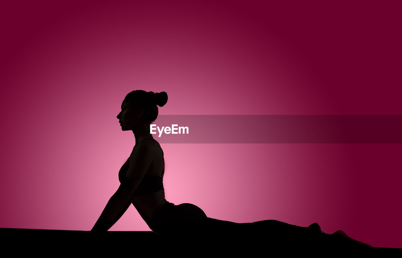Silhouette woman doing yoga on pink background