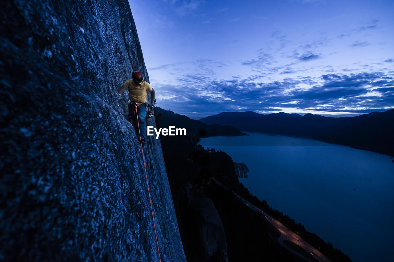 Side view man rock climbing at night above the sea and highway