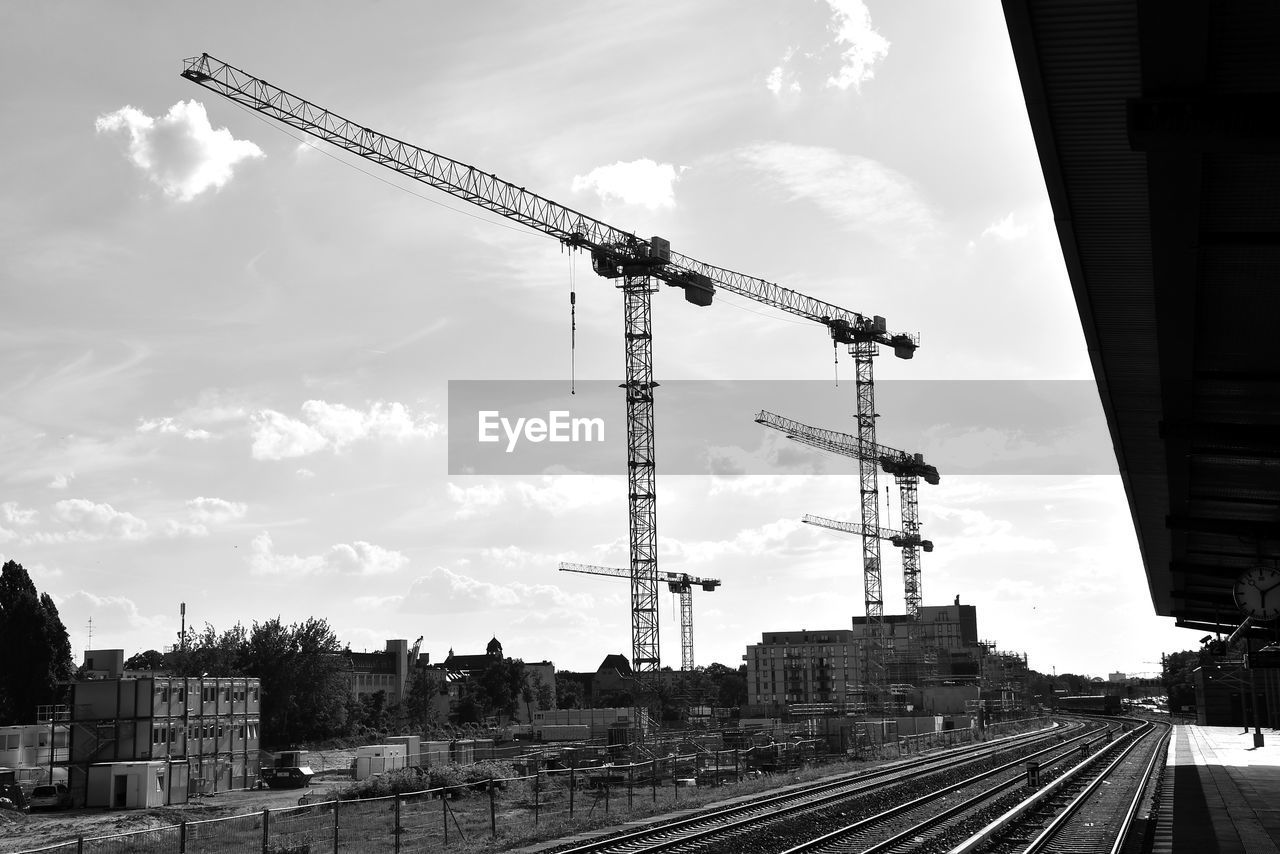 architecture, sky, crane - construction machinery, built structure, cloud, transport, machinery, track, transportation, railroad track, rail transportation, black and white, building exterior, construction industry, city, industry, monochrome, vehicle, nature, construction site, monochrome photography, development, mode of transportation, no people, outdoors, travel, business finance and industry, day, electricity, train, business
