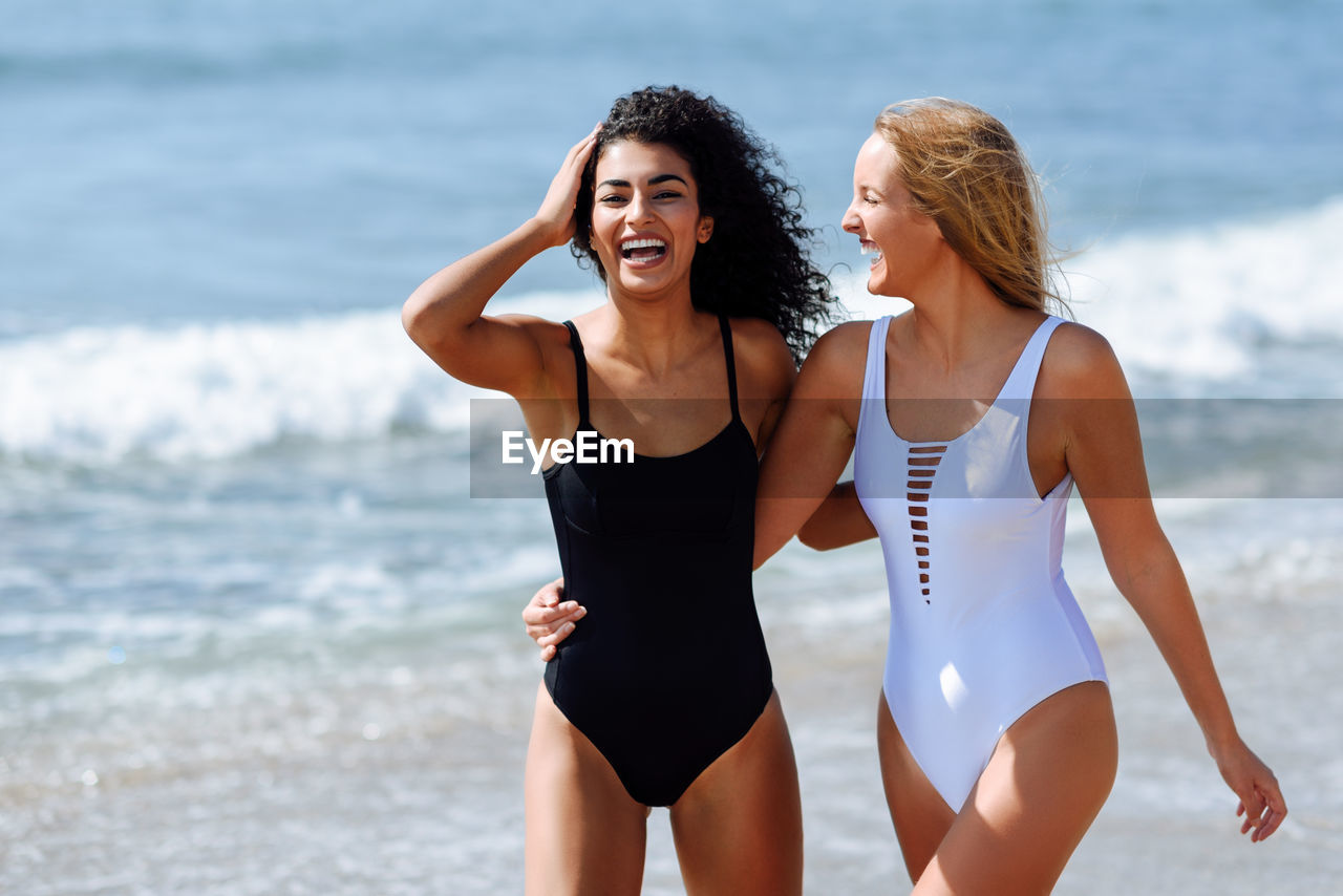 Portrait of smiling young woman with friend standing at beach