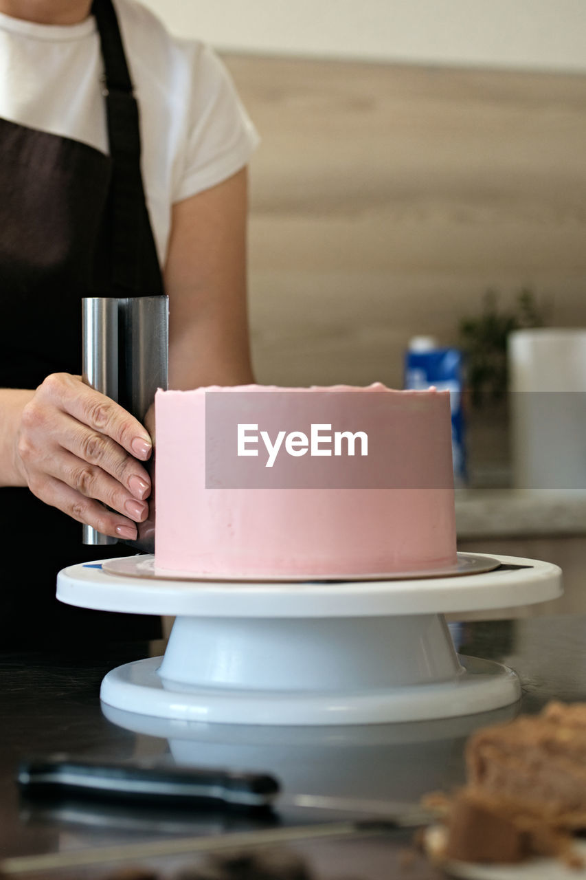 Woman pastry chef making chocolate cake with pink cream, close-up. cake making process