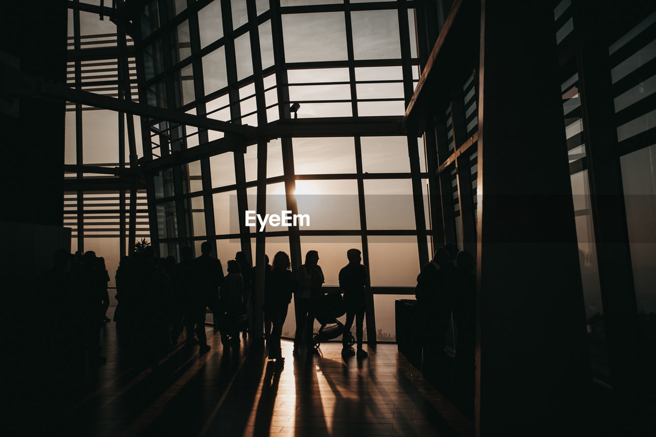 Silhouette of people standing by window during sunset