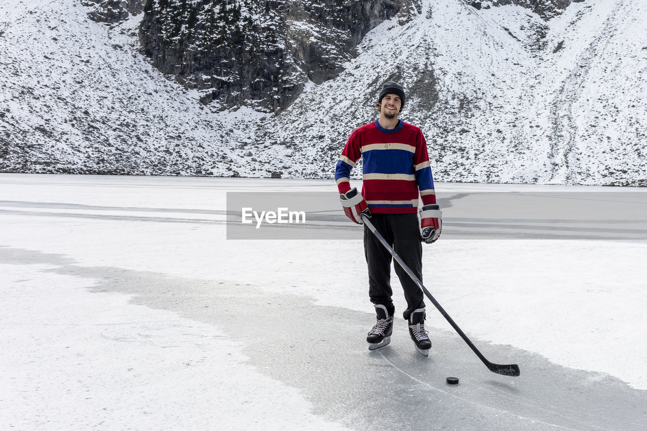 Happy hockey player on frozen lake with stick and puck while smiling