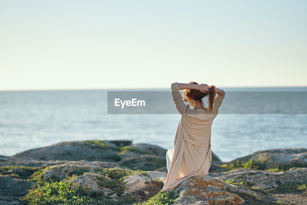 Person on rock by sea against clear sky