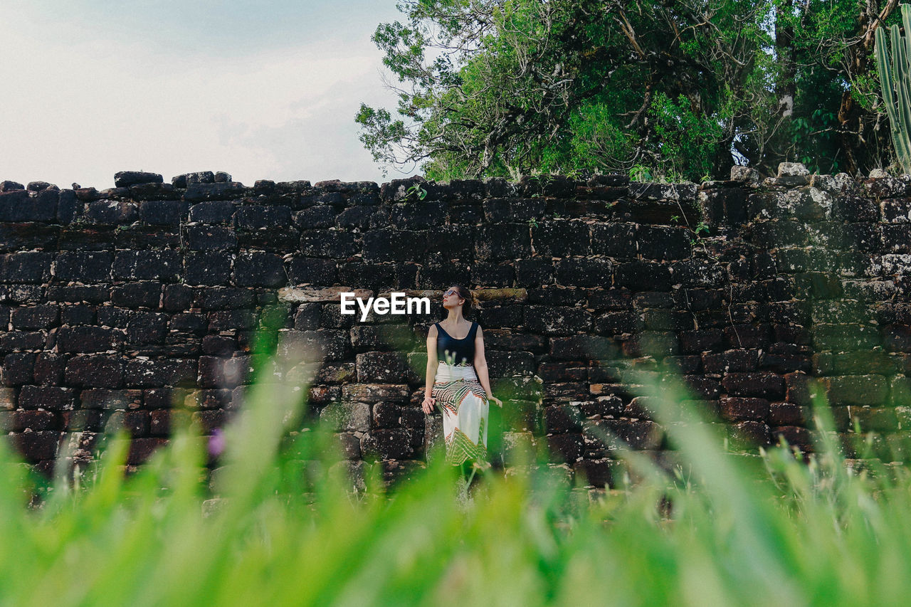 Full length of woman sitting against stone wall