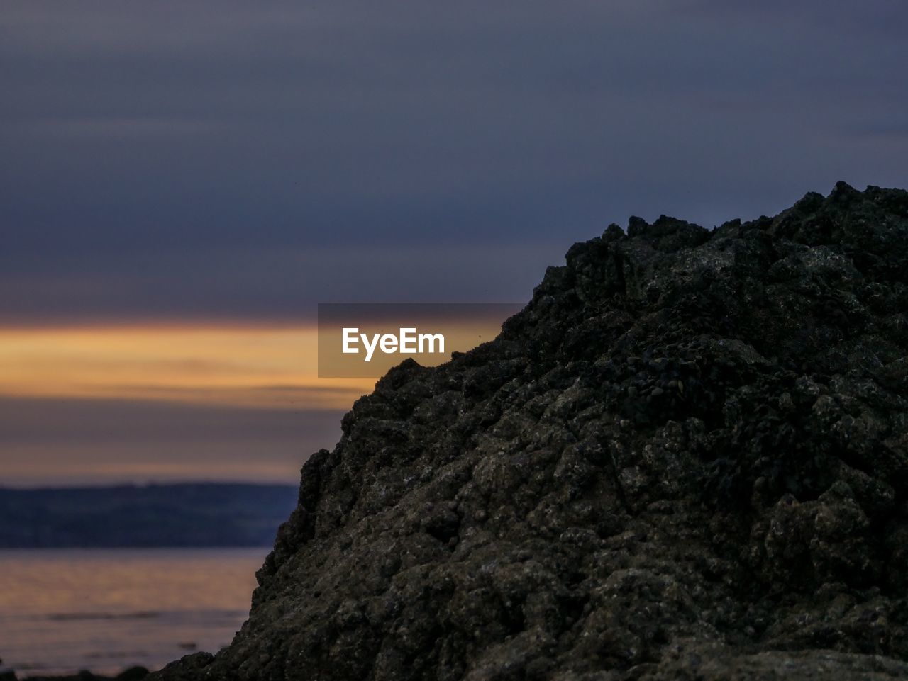 Rock formation by sea against sky during sunset