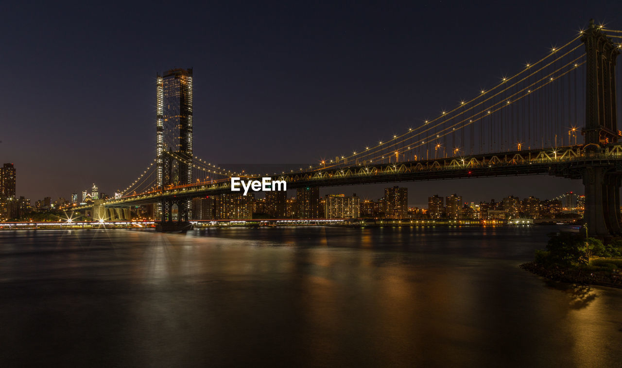 Illuminated bridge over river in city at night