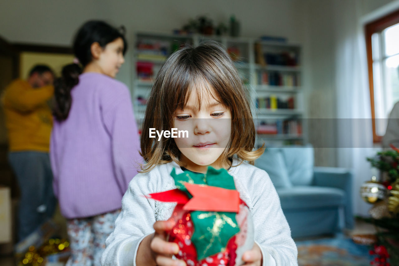 Little child holds christmas decoration in hands with family behind