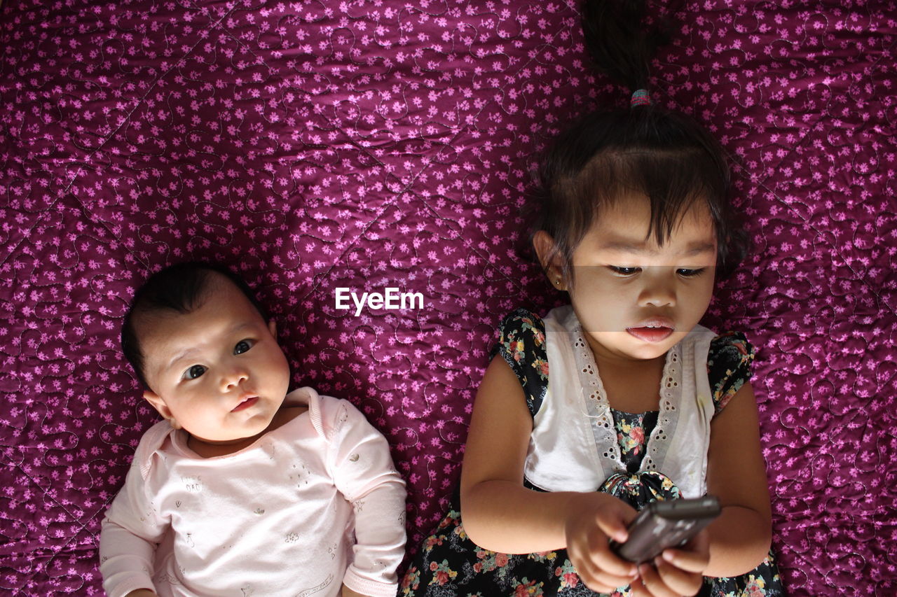 Directly above shot of cute brother and sister lying on purple blanket