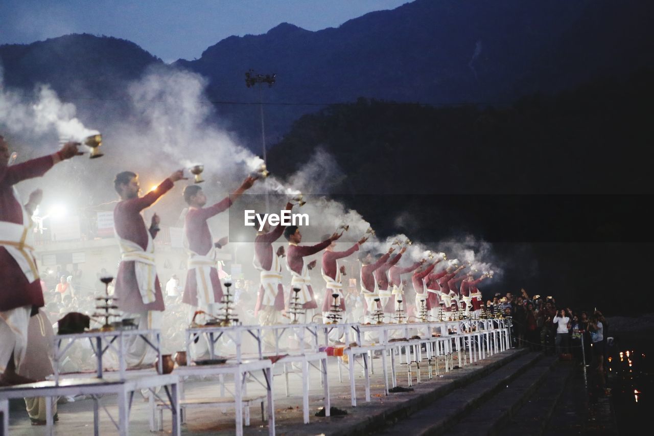 People performing ganga aarti ceremony held on edge of ganges river against sky