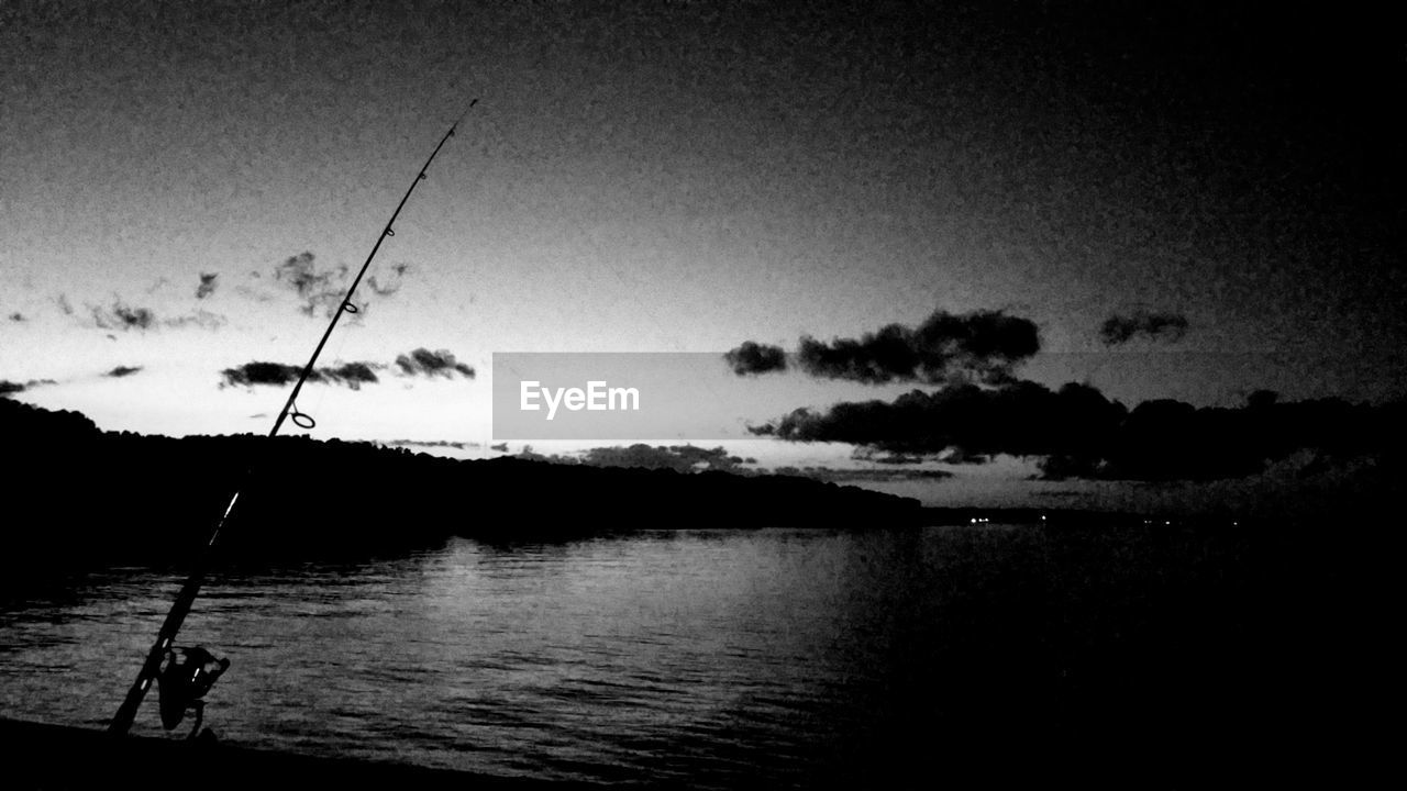 Silhouette fishing rod by lake against sky
