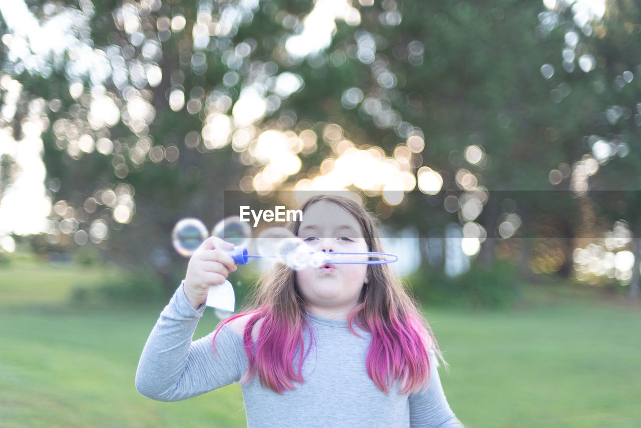 Portrait of girl blowing bubbles in park