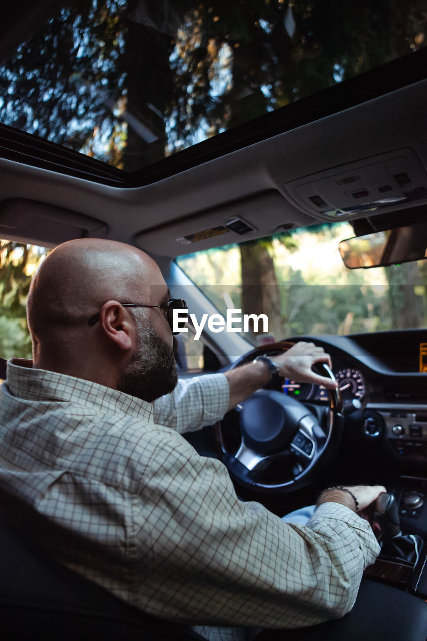 Brutal bald bearded middle-aged man drives a car