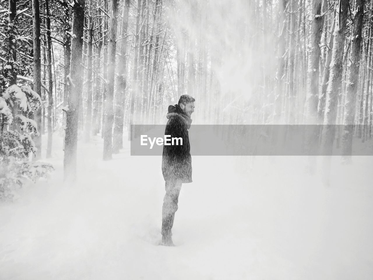 Side view of man standing on snow covered field amidst tree