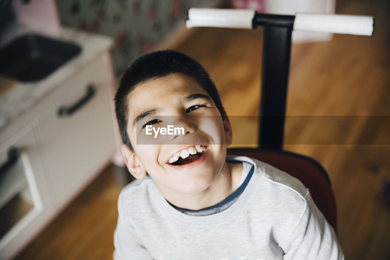 High angle view of happy disabled boy sitting on wheelchair at home