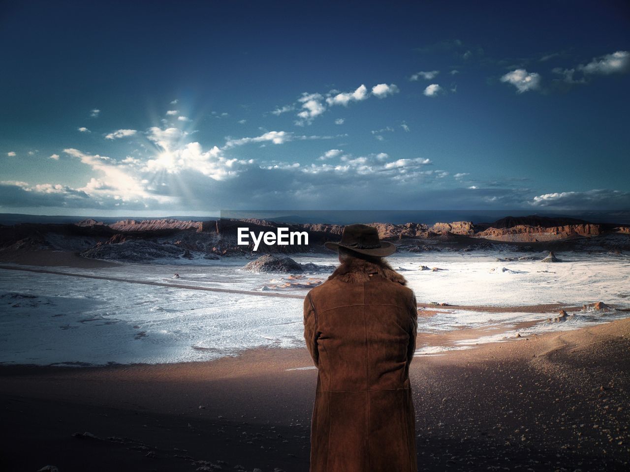 Rear view of man looking at landscape against sky during winter