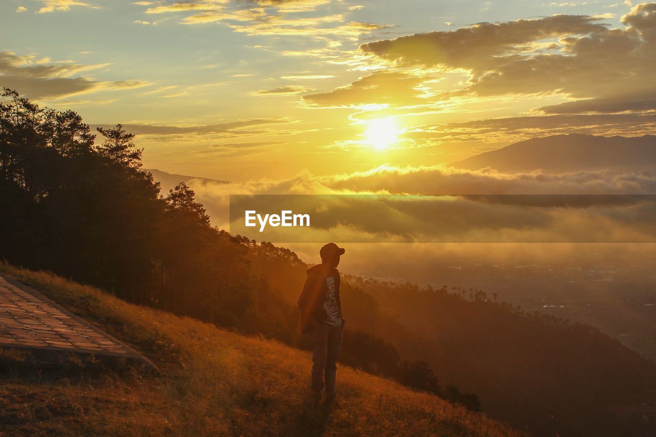 Man standing on mountain peak while looking at sky during sunrise