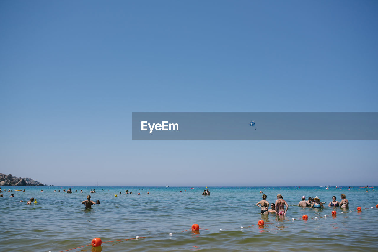 People in sea against clear blue sky