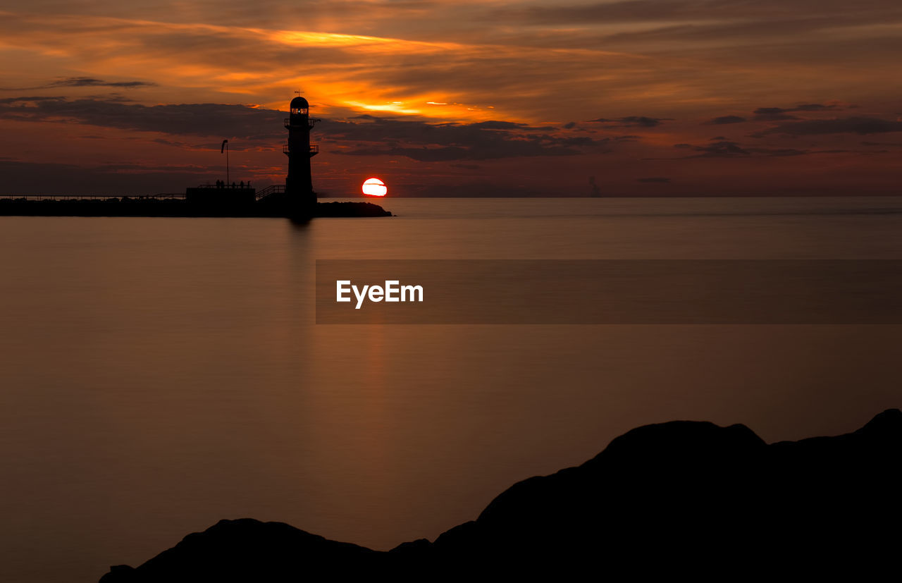 Silhouette lighthouse by sea against sky during sunset