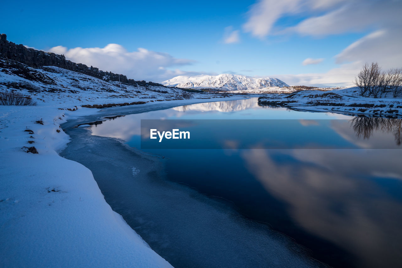 Frozen lake by mountain against sky during winter