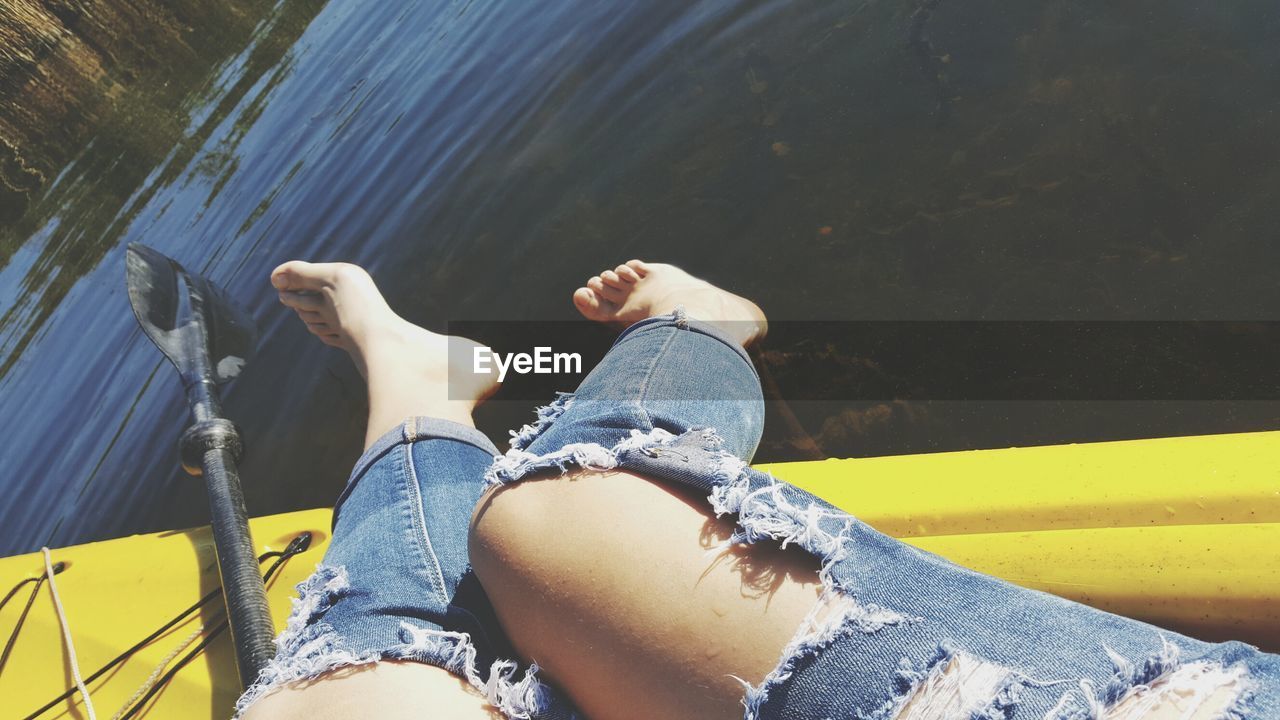 Low section of woman wearing torn jeans sitting on boat in lake