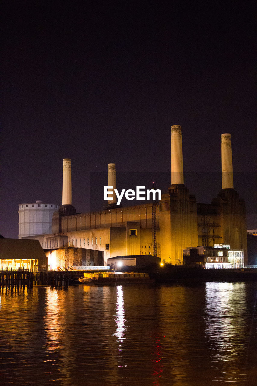 Illuminated battersea power station by thames river against sky