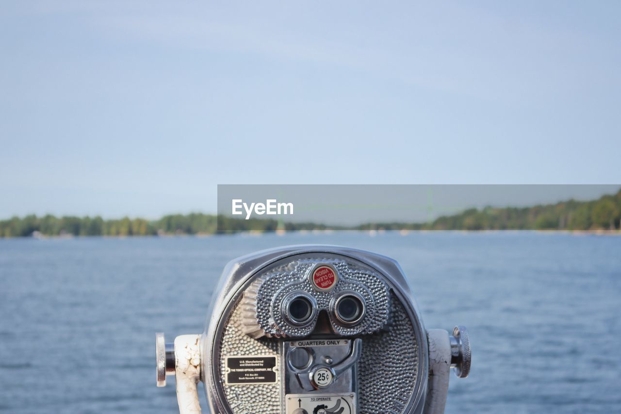 Close-up of coin-operated binoculars by sea against sky