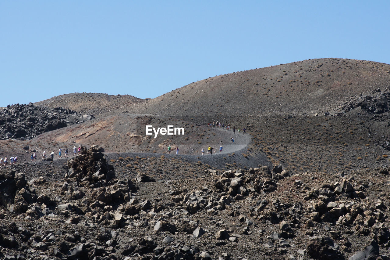 Group of people walking on barren landscape against blue sky