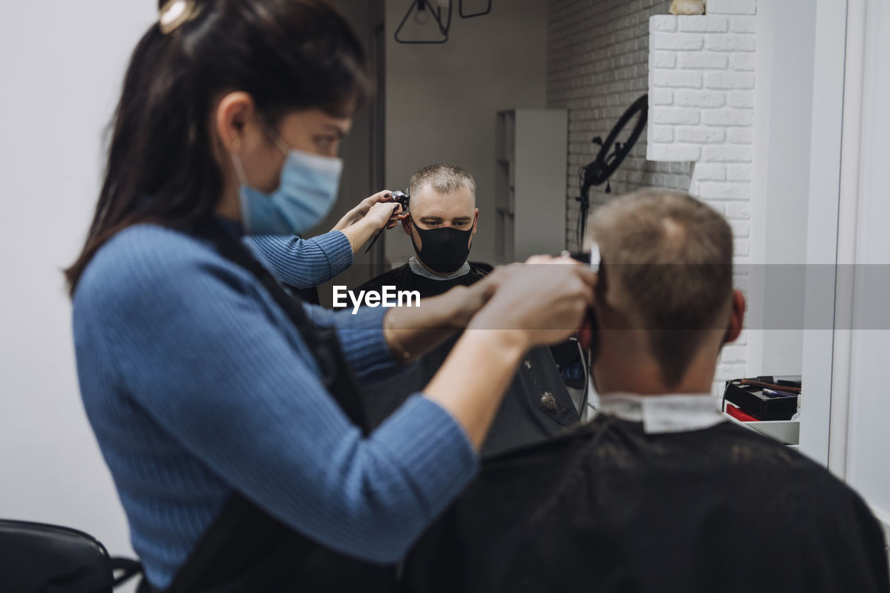 Female barber cutting hair of customer in saloon