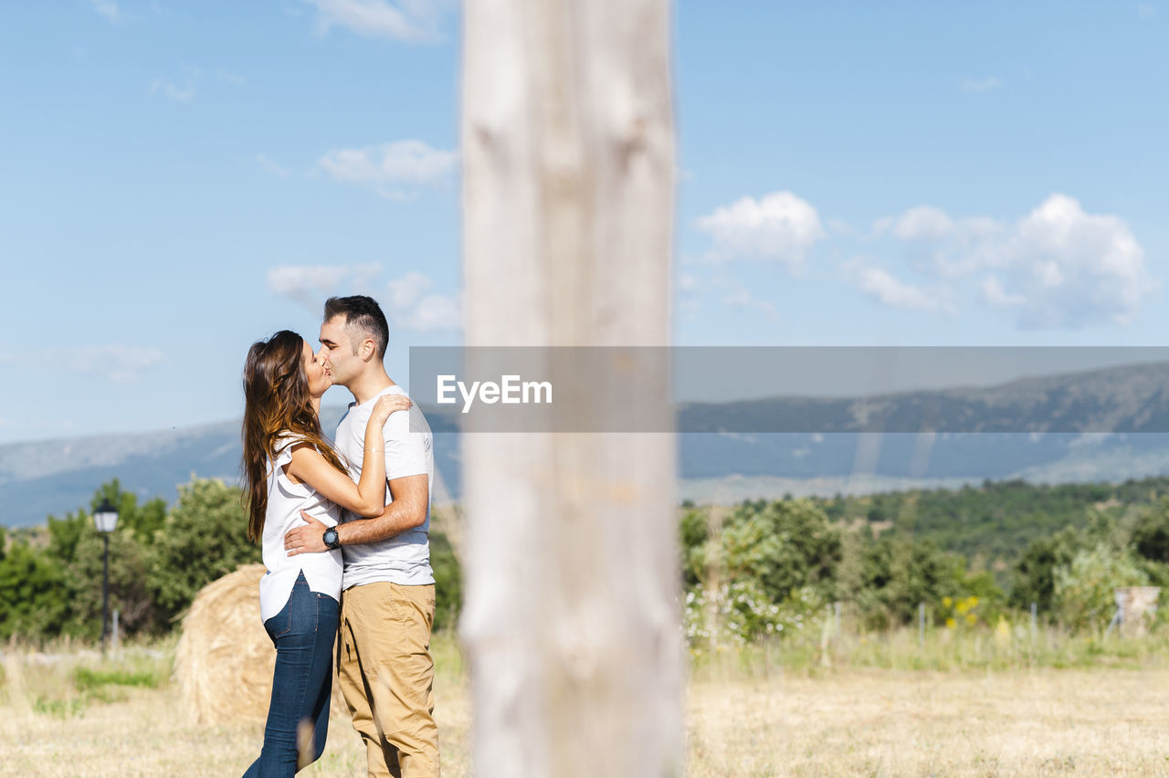 Young couple kissing on agricultural field during sunny day